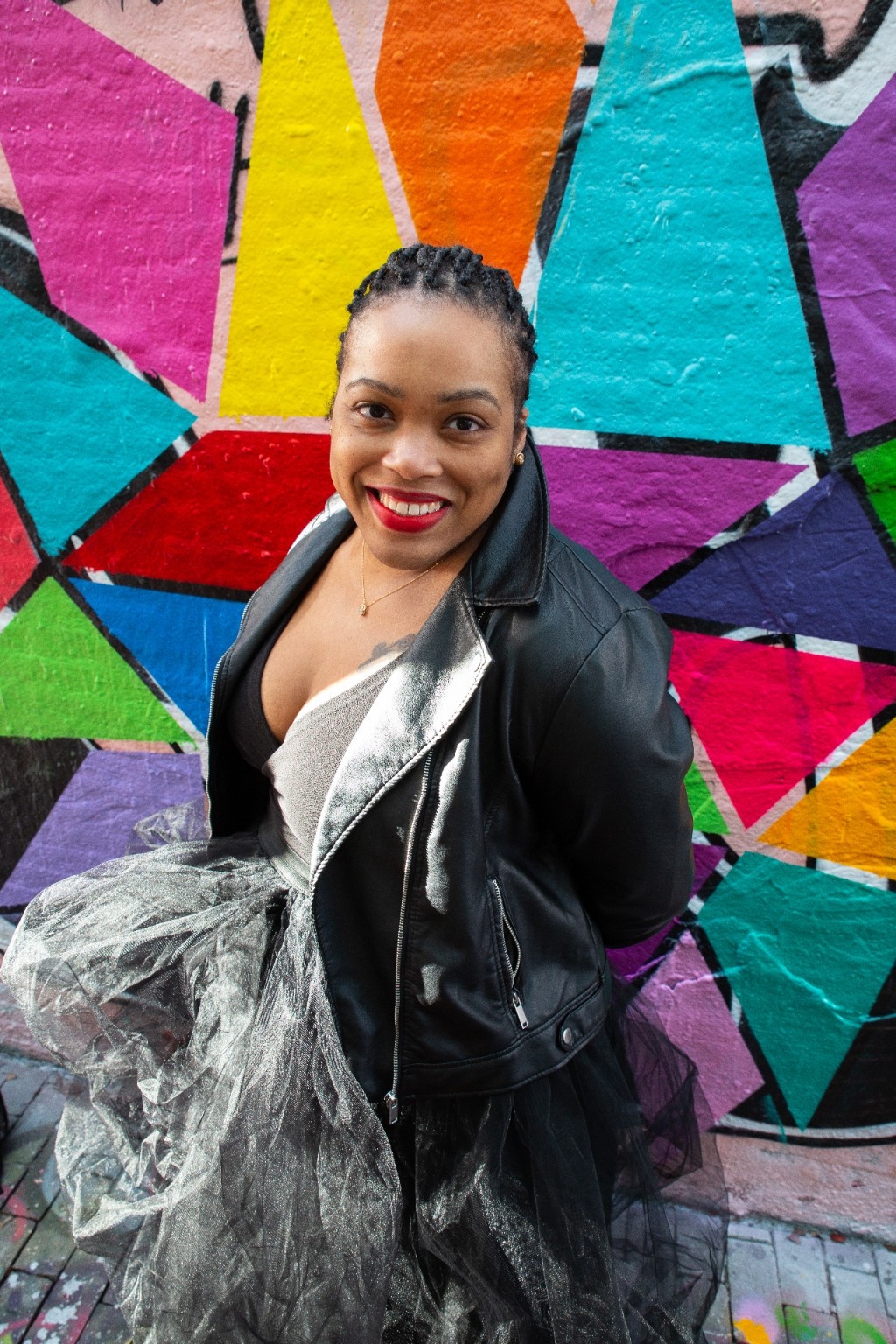 Rica Elysée smiling in front of a colorful geometric mural